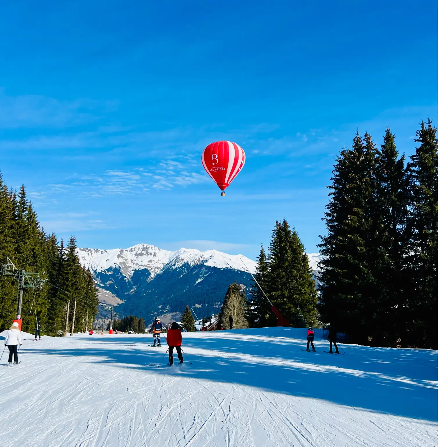 Skiers on a slope with a hot air balloon in the sky over Courchevel