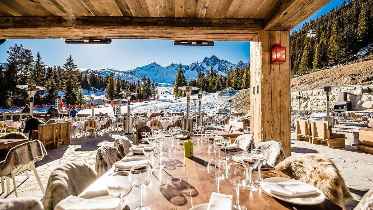 Long table laid on a sun-lit mountain terrace in Courchevel, fur throws on the chairs and snow-covered peaks beyond